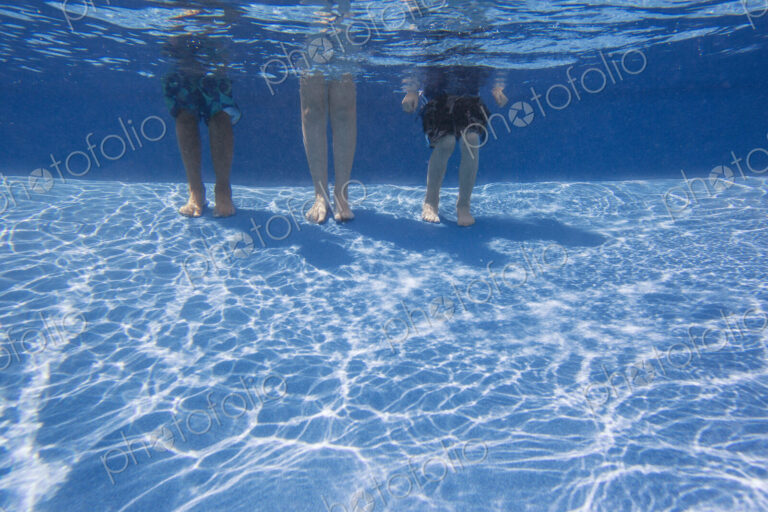 Three people standing on the bottom of a swimming pool. View from the knees down.