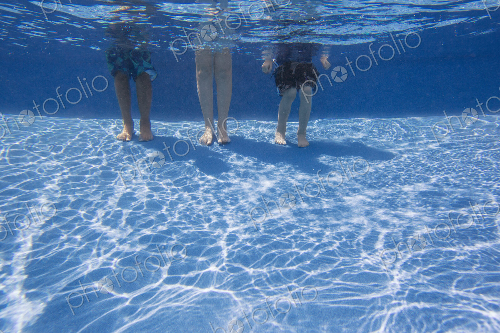 Three people standing on the bottom of a swimming pool. View from the knees down.