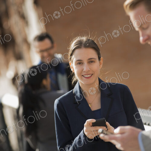 Three people standing on the sidewalk in the city, checking their phones. Two men and… Three people standing on the sidewalk in the city, checking their phones. Two men and…