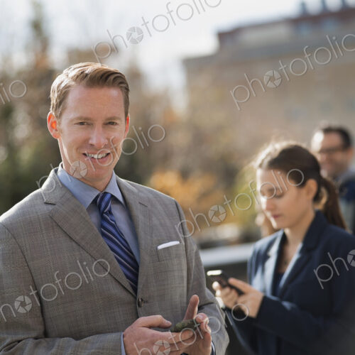 Three people standing on the sidewalk in the city, checking their phones. Two men and… Three people standing on the sidewalk in the city, checking their phones. Two men and…