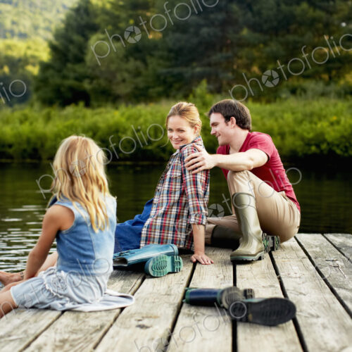 Three people, two adults and a child relaxing on a jetty, with their feet in the water… Three people, two adults and a child relaxing on a jetty, with their feet in the water…