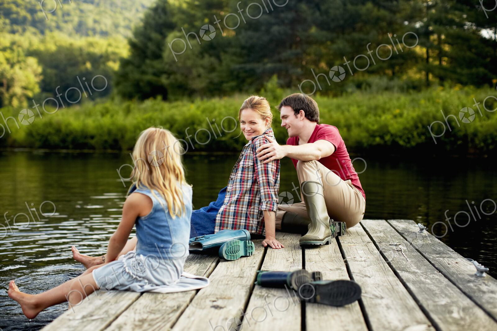 Three people, two adults and a child relaxing on a jetty, with their feet in the water…