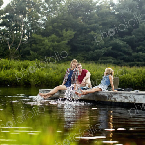 Three people, two adults and a child relaxing on a jetty, with their feet in the water… Three people, two adults and a child relaxing on a jetty, with their feet in the water…