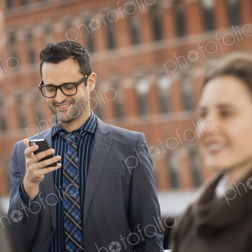 Three people, two in the foreground, and a man looking at a cell phone display. Three people, two in the foreground, and a man looking at a cell phone display.