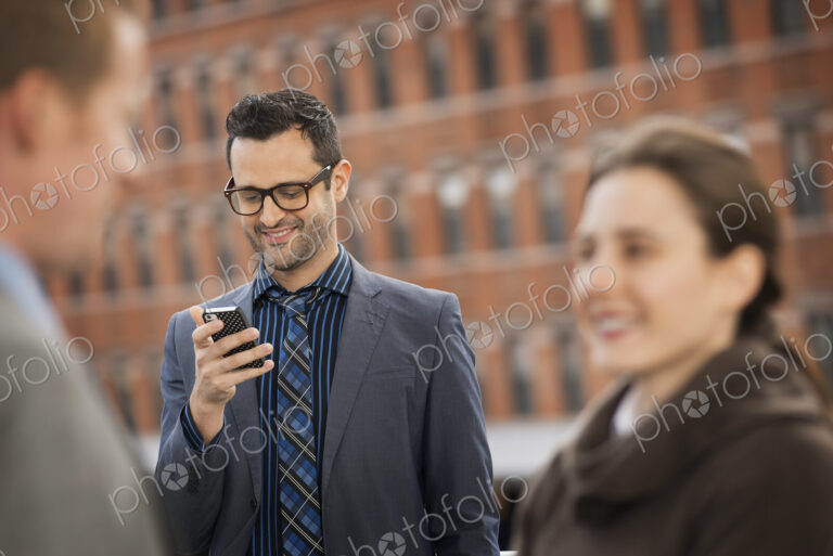 Three people, two in the foreground, and a man looking at a cell phone display.
