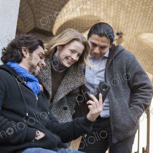 Three people, two men and a woman looking at the screen of a smart phone. Three people, two men and a woman looking at the screen of a smart phone.