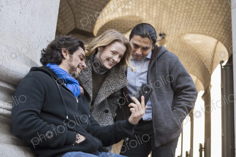 Three people, two men and a woman looking at the screen of a smart phone.