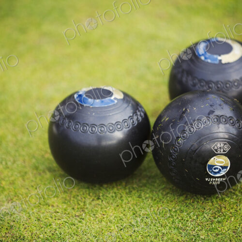 Three round wooden black lawn bowls on a smooth playing surface.