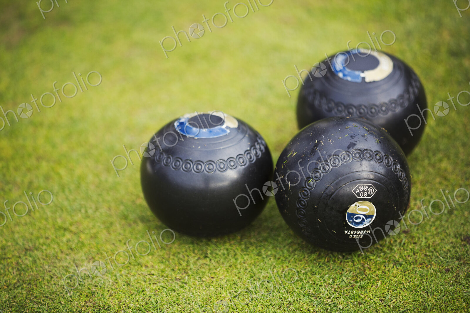 Three round wooden black lawn bowls on a smooth playing surface.
