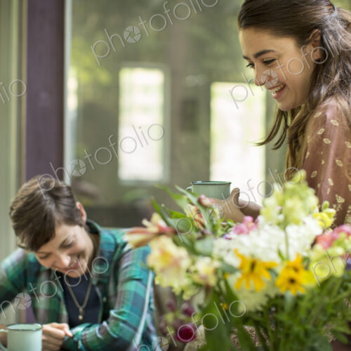 Three women talking and laughing, seated around a table. Large bunch of flowers in a vase. Three women talking and laughing, seated around a table. Large bunch of flowers in a vase.