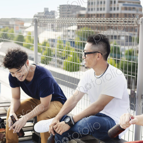 Three young Japanese men sitting on a rooftop in an urban setting, drinking beer. Three young Japanese men sitting on a rooftop in an urban setting, drinking beer.