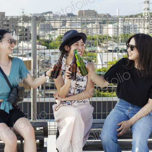 Three young Japanese women sitting on a rooftop in an urban setting, drinking beer. Three young Japanese women sitting on a rooftop in an urban setting, drinking beer.