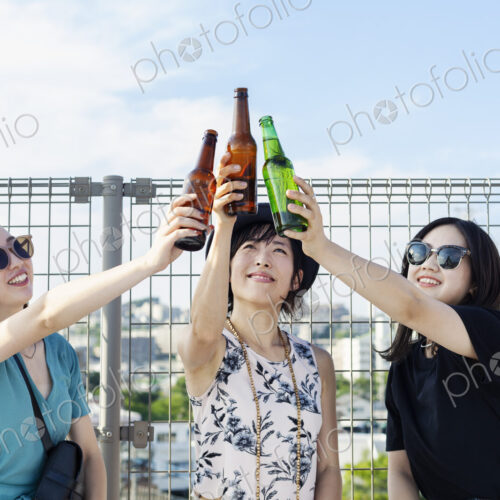 Three young Japanese women sitting on a rooftop in an urban setting, drinking beer. Three young Japanese women sitting on a rooftop in an urban setting, drinking beer.