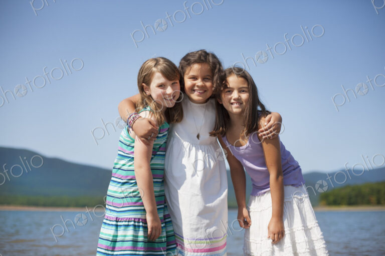 Three young girls, friends, hugging each other and smiling.