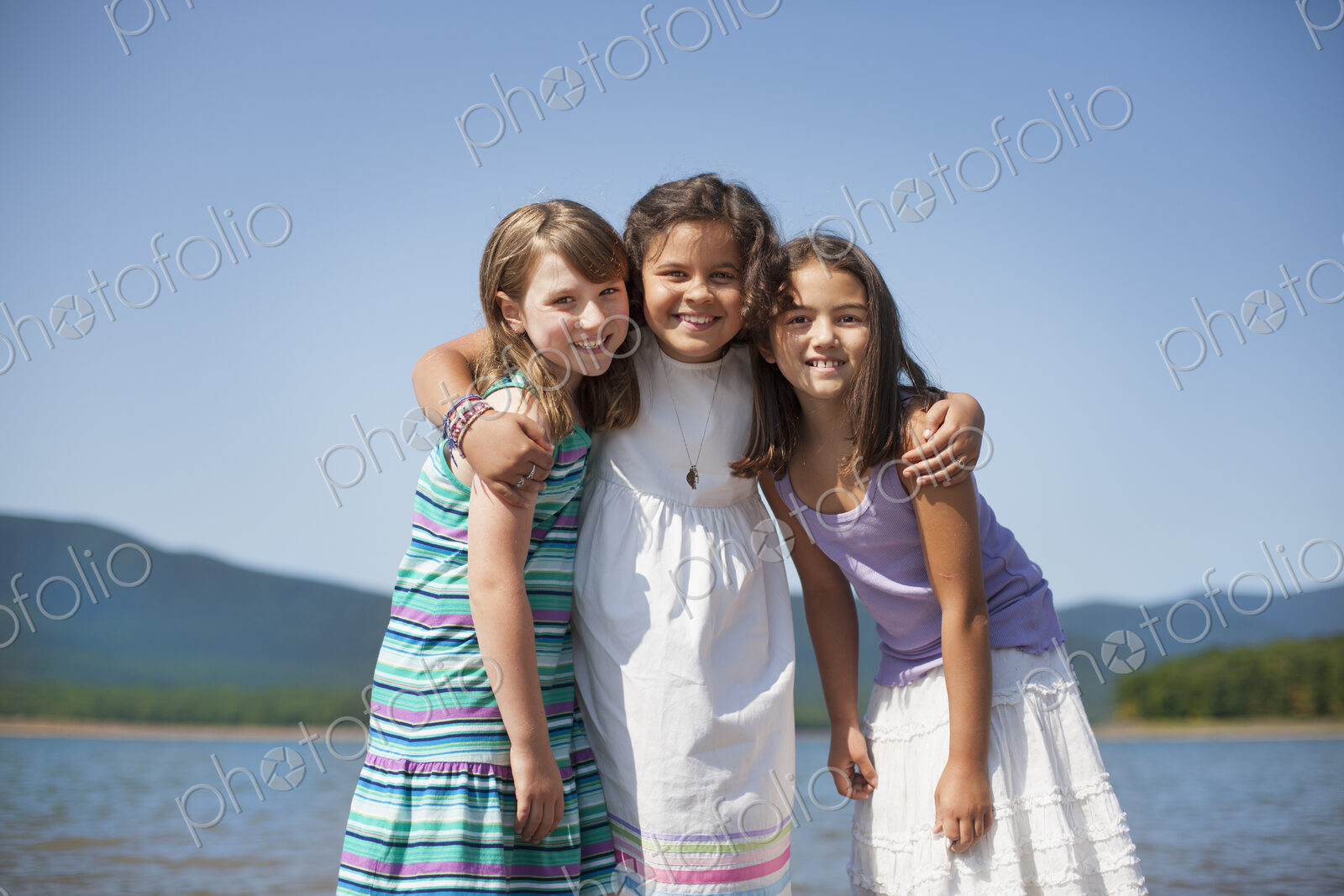 Three young girls, friends, hugging each other and smiling.