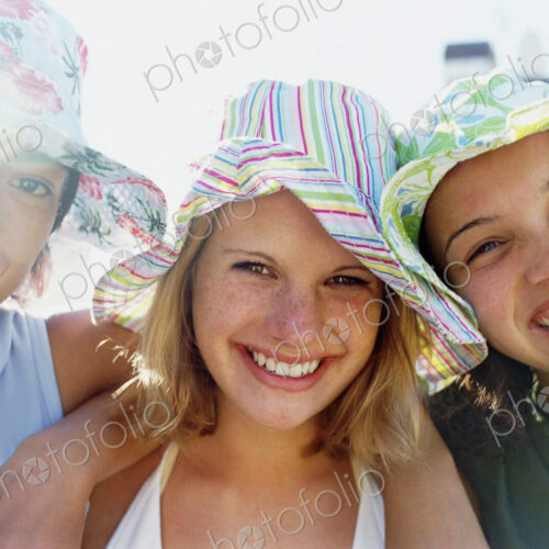 Three young girls in a row wearing sunhats looking at the camera and smiling.