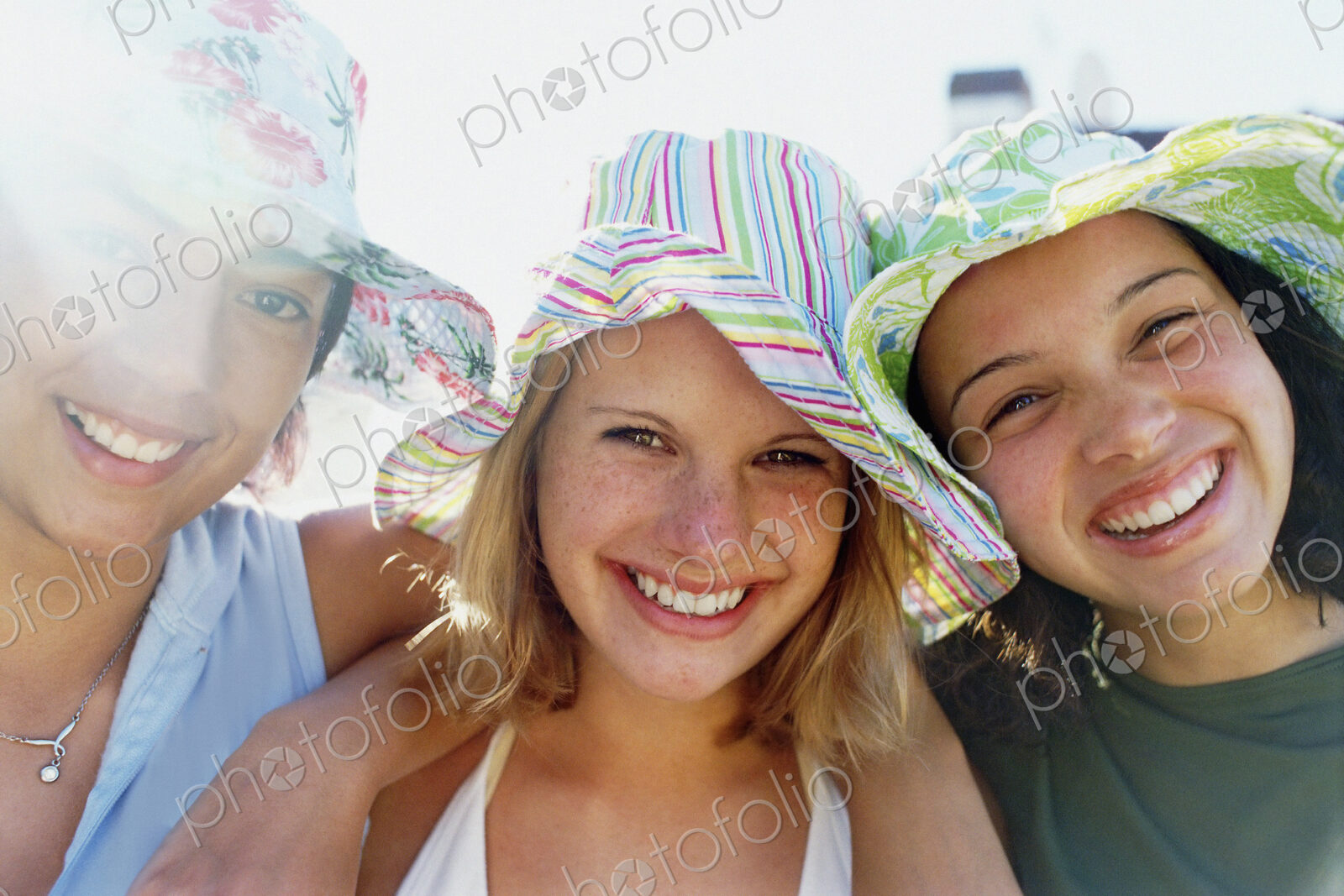 Three young girls in a row wearing sunhats looking at the camera and smiling.