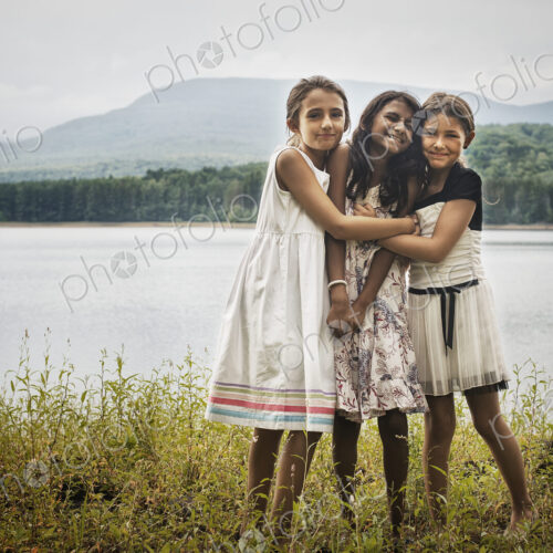 Three young girls standing by the side of a lake, hugging each other. Three young girls standing by the side of a lake, hugging each other.