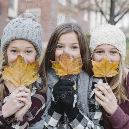 Three young girls standing in a row, holding autumn leaves in front of their faces. Three young girls standing in a row, holding autumn leaves in front of their faces.