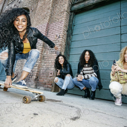 Three young women with curly hair squatting in front of shutter, watching smiling… Three young women with curly hair squatting in front of shutter, watching smiling…