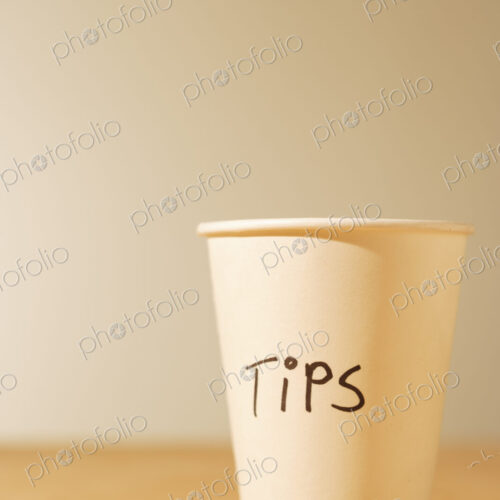 Tips cup, a white paper cup for gratuities on a table.