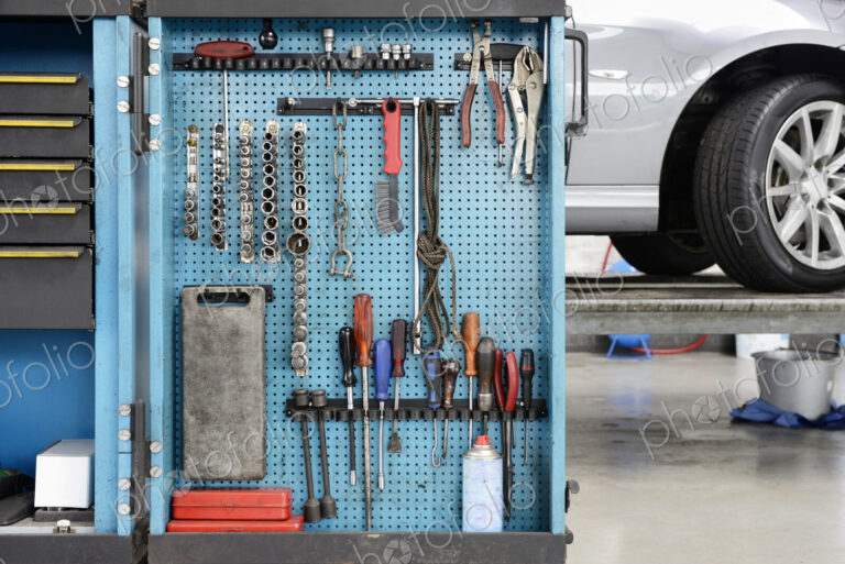 Tools on a blue board in a storage cabinet,organised in rows,at an auto repair shop.