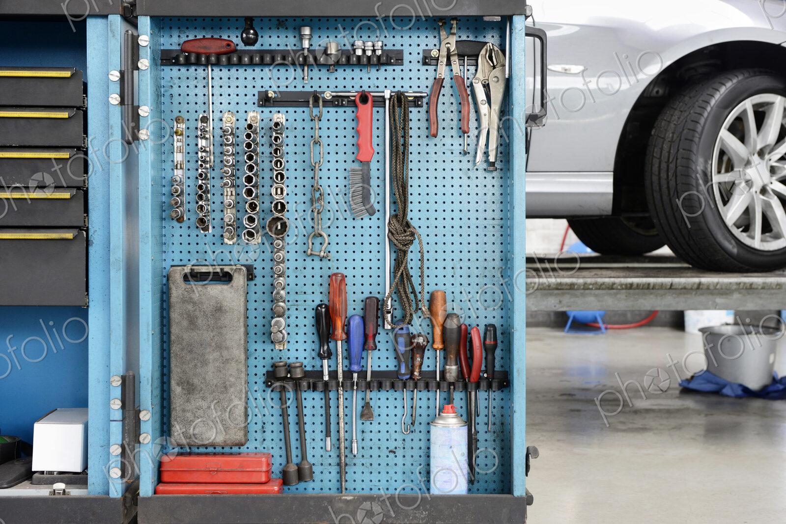 Tools on a blue board in a storage cabinet,organised in rows,at an auto repair shop.