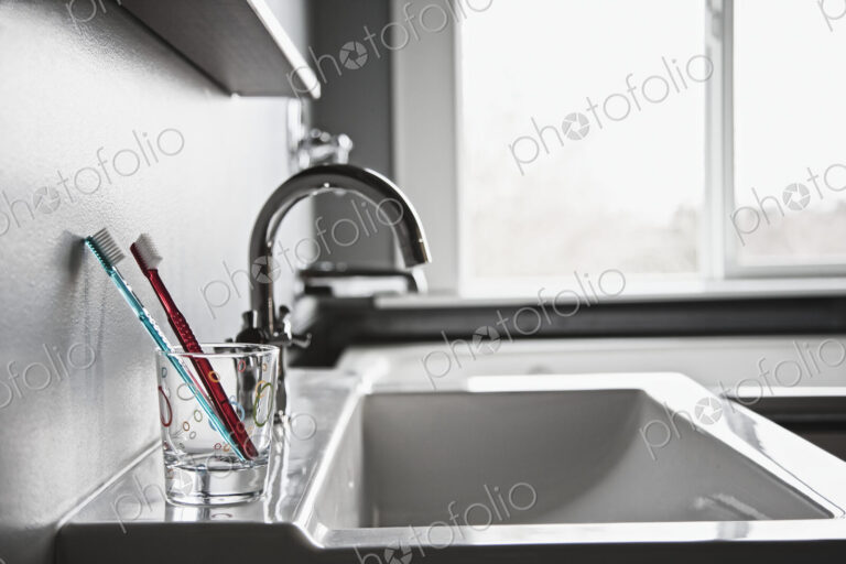 Toothbrushes in drinking glass in domestic bathroom.