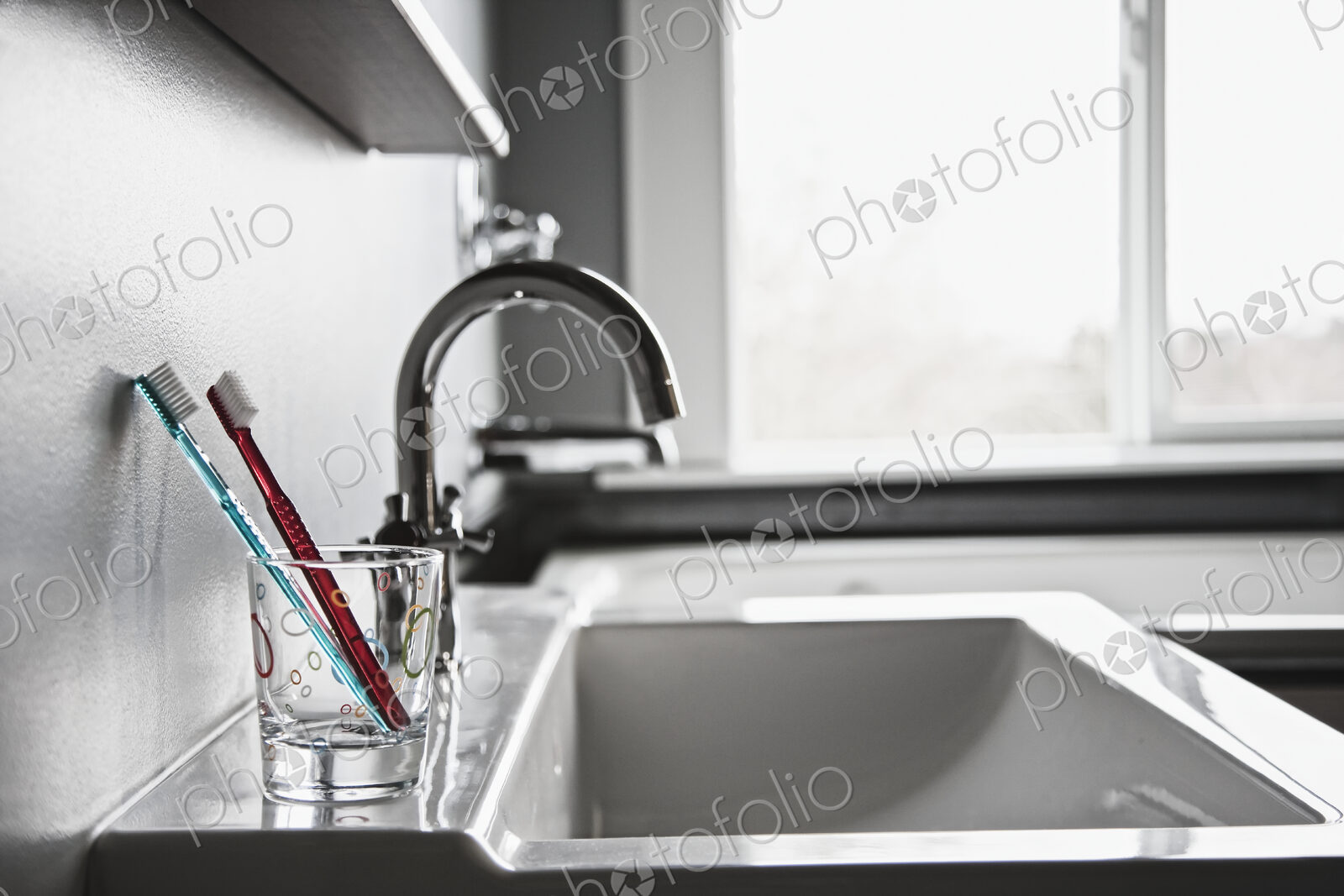Toothbrushes in drinking glass in domestic bathroom.