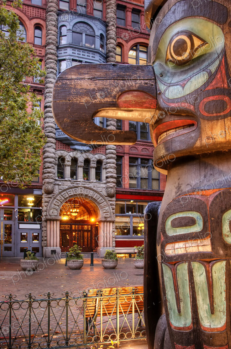 Totem pole on street with historic apartment building behind.
