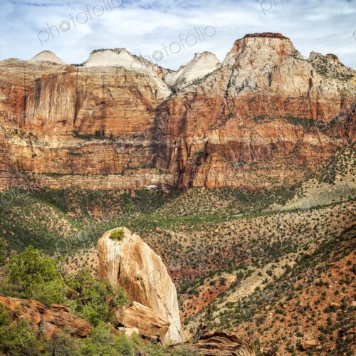Towering red and white sandstone cliffs rise above rugged desert terrain and green… Towering red and white sandstone cliffs rise above rugged desert terrain and green…