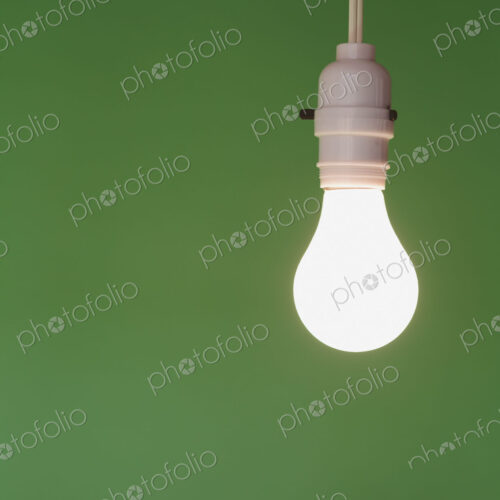 Traditional glass light bulb and switch with a white electric flex. Green background.
