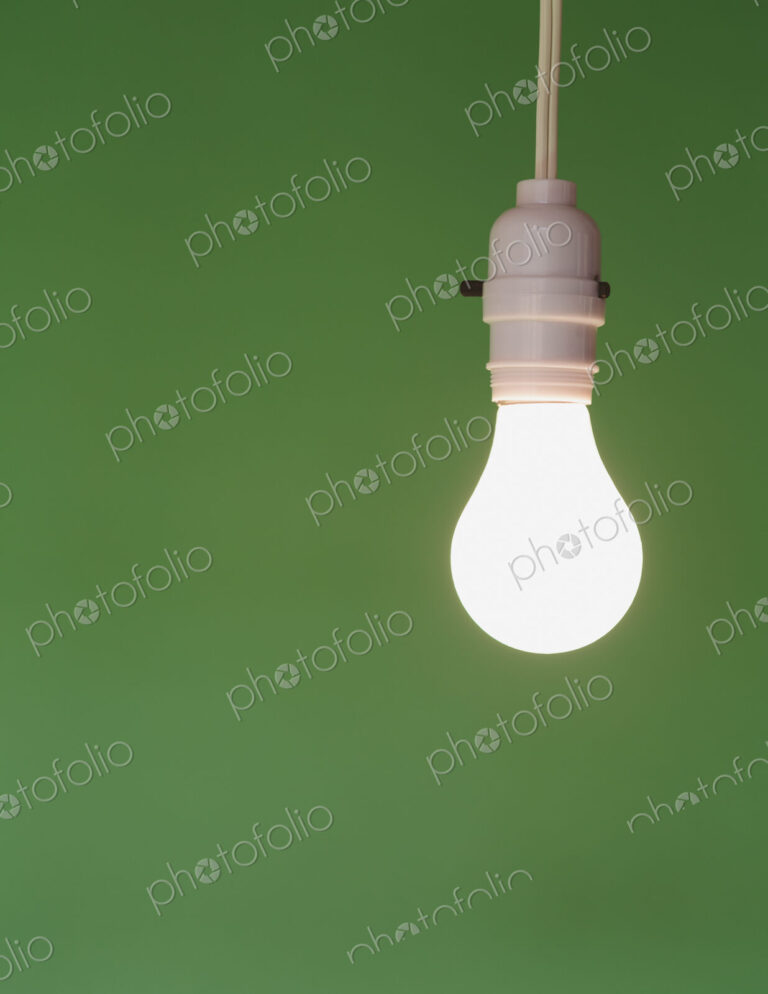 Traditional glass light bulb and switch with a white electric flex. Green background.