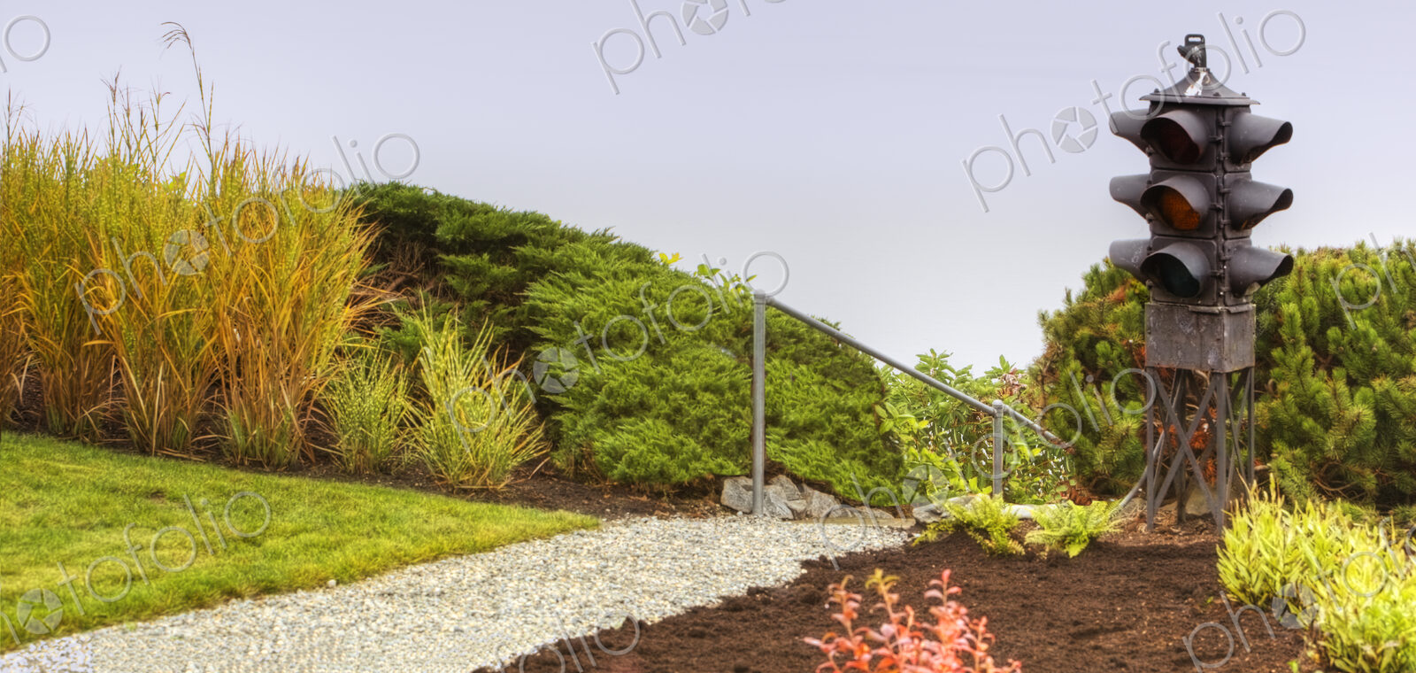 Traffic light in a garden, flower border with shrubs and path.