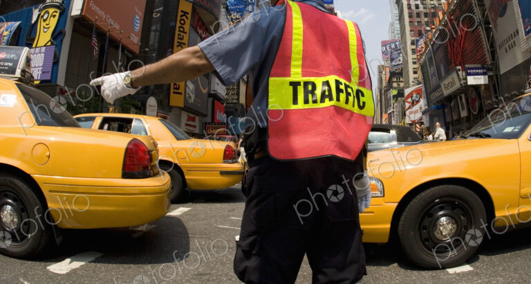 Traffic officer directing rush hour traffic on urban street, yellow cabs passing.