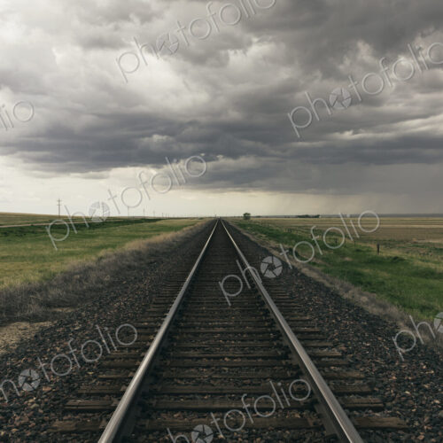 Train tracks through prairie and farmland, storm clouds in distance