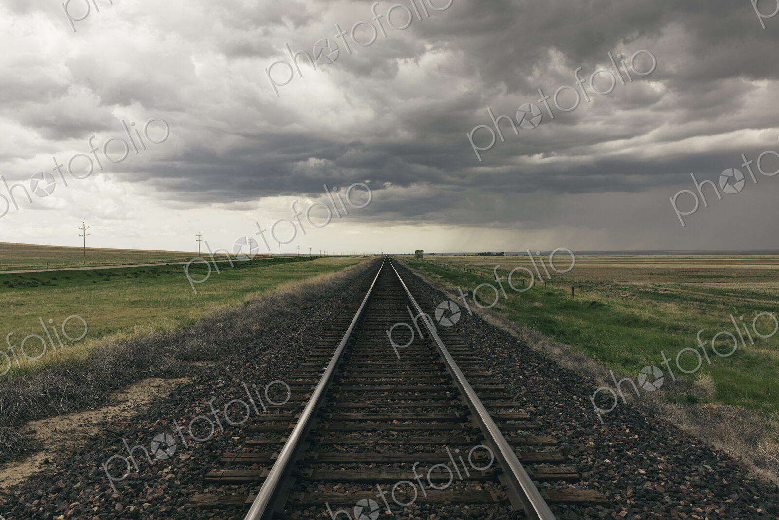 Train tracks through prairie and farmland, storm clouds in distance