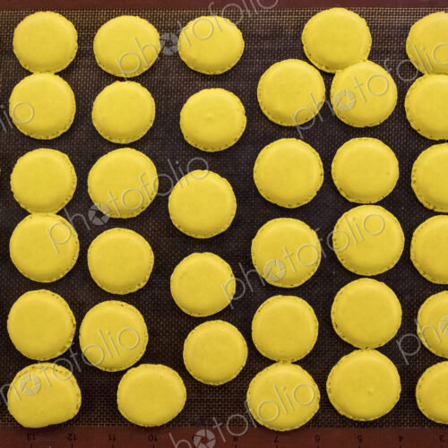 Trays of small round yellow baked biscuits or macarons. Overhead view. Trays of small round yellow baked biscuits or macarons. Overhead view.