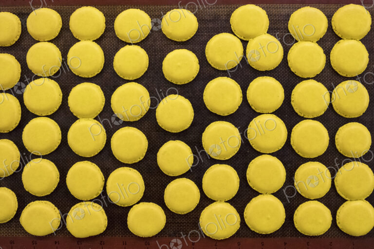 Trays of small round yellow baked biscuits or macarons. Overhead view.