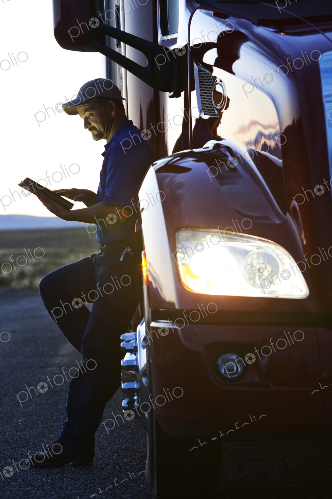 Truck driver checking his notebook computer log while standing next to the cab of his…