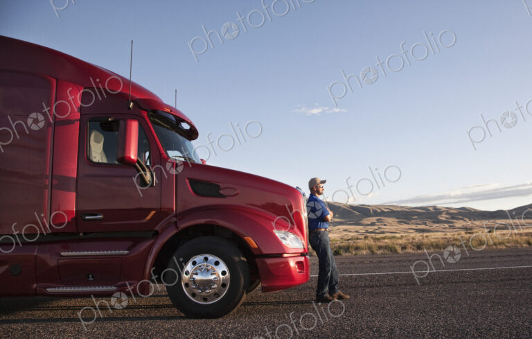 Truck driver leaning on the grill of his commercial truck.