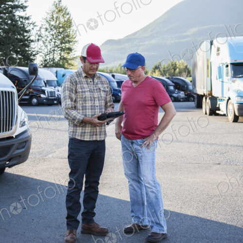 Truck driver team of caucasian drivers going over dispatch information in the parking… Truck driver team of caucasian drivers going over dispatch information in the parking…