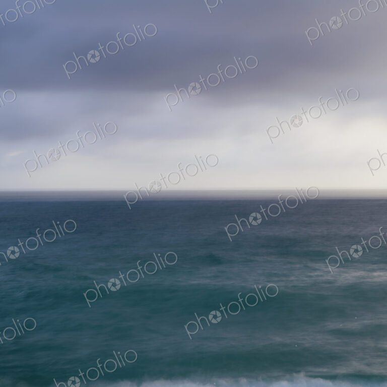 Turquoise ocean surface under a grey stormy sky.