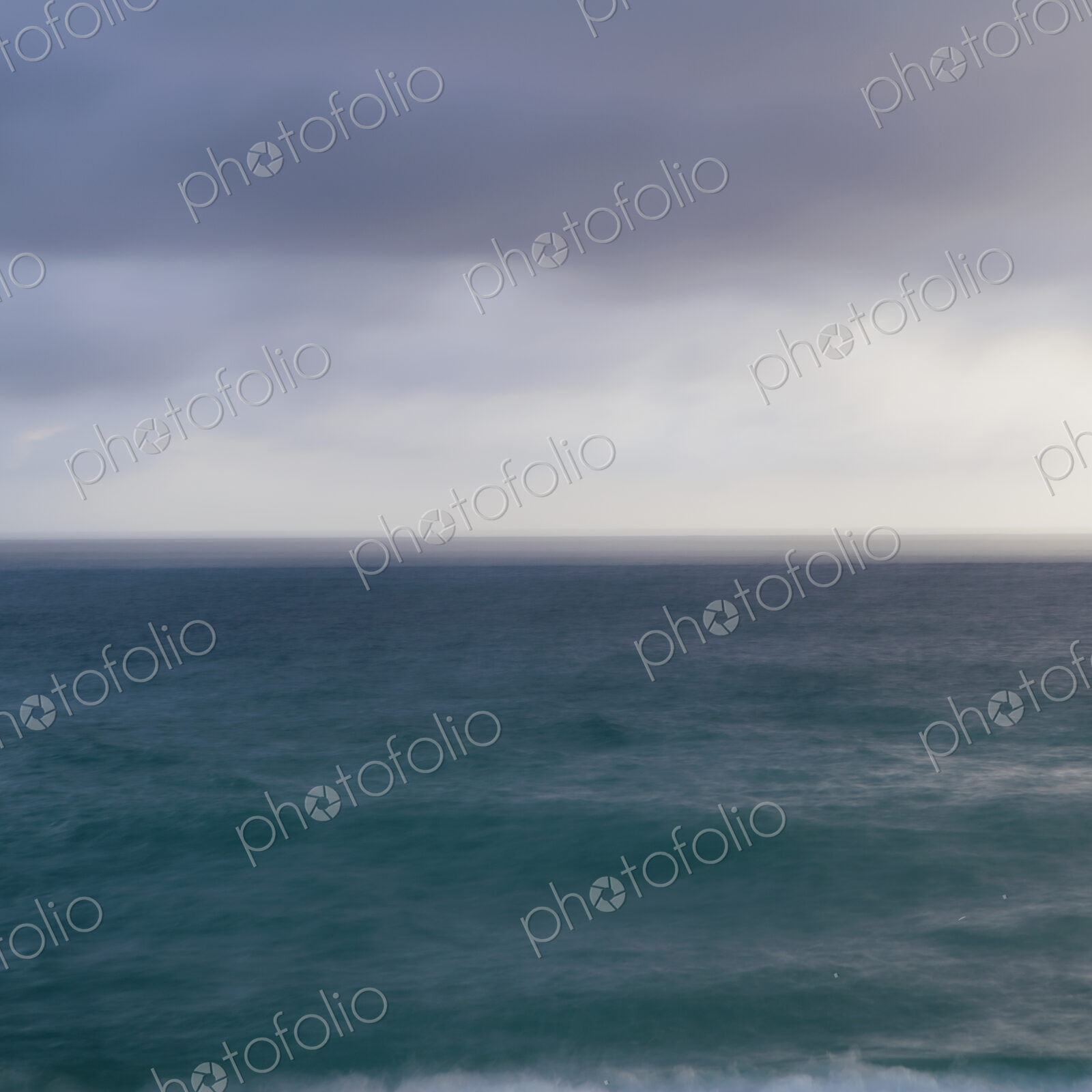 Turquoise ocean surface under a grey stormy sky.