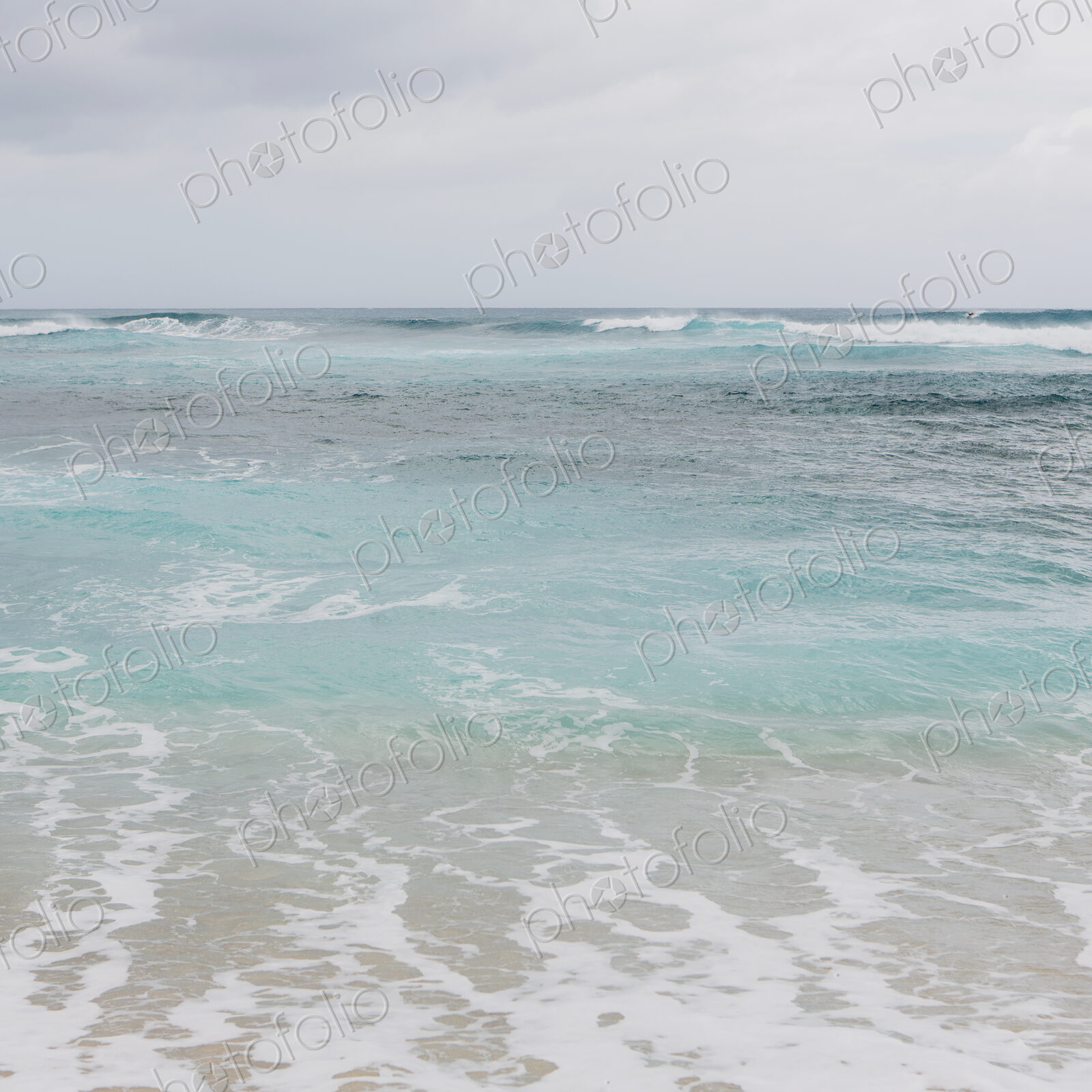 Turquoise ocean water, waves on the beach and an overcast sky.