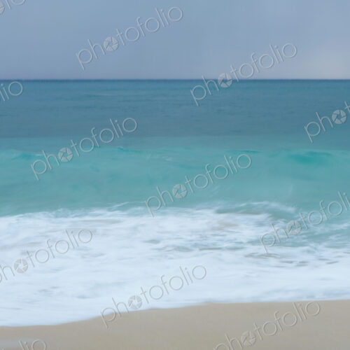 Turquoise sea, waves breaking on a sandy beach.