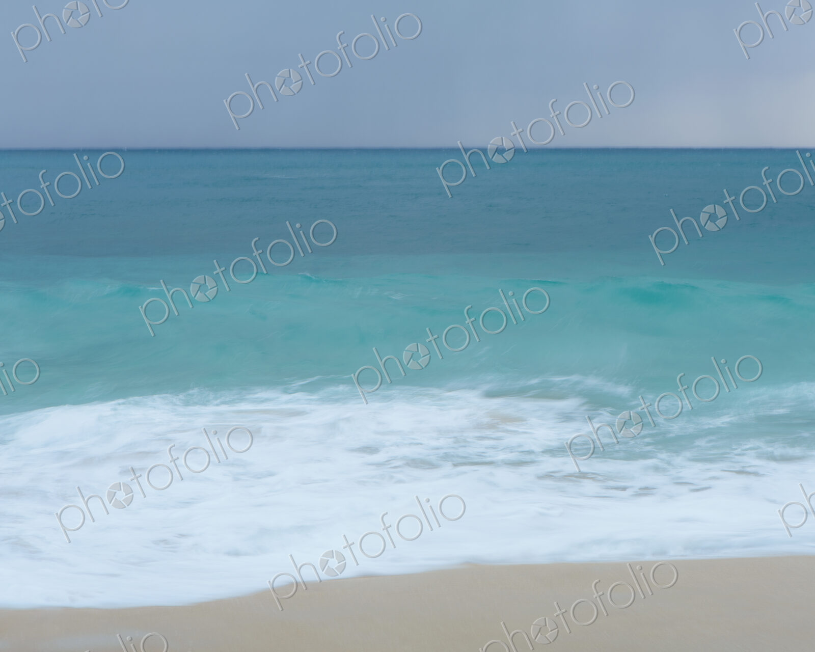 Turquoise sea, waves breaking on a sandy beach.