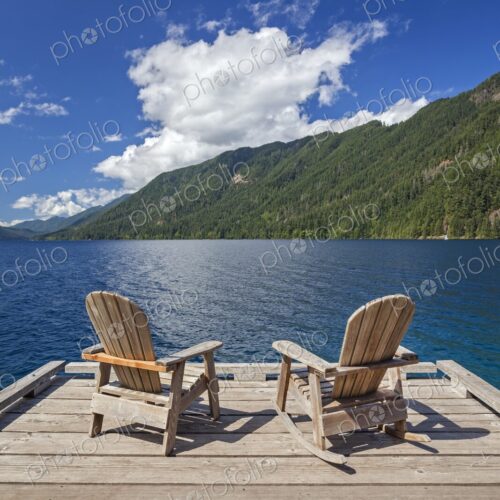 Two Adirondack chairs rest on a wooden dock with views of Lake Crescent and… Two Adirondack chairs rest on a wooden dock with views of Lake Crescent and…