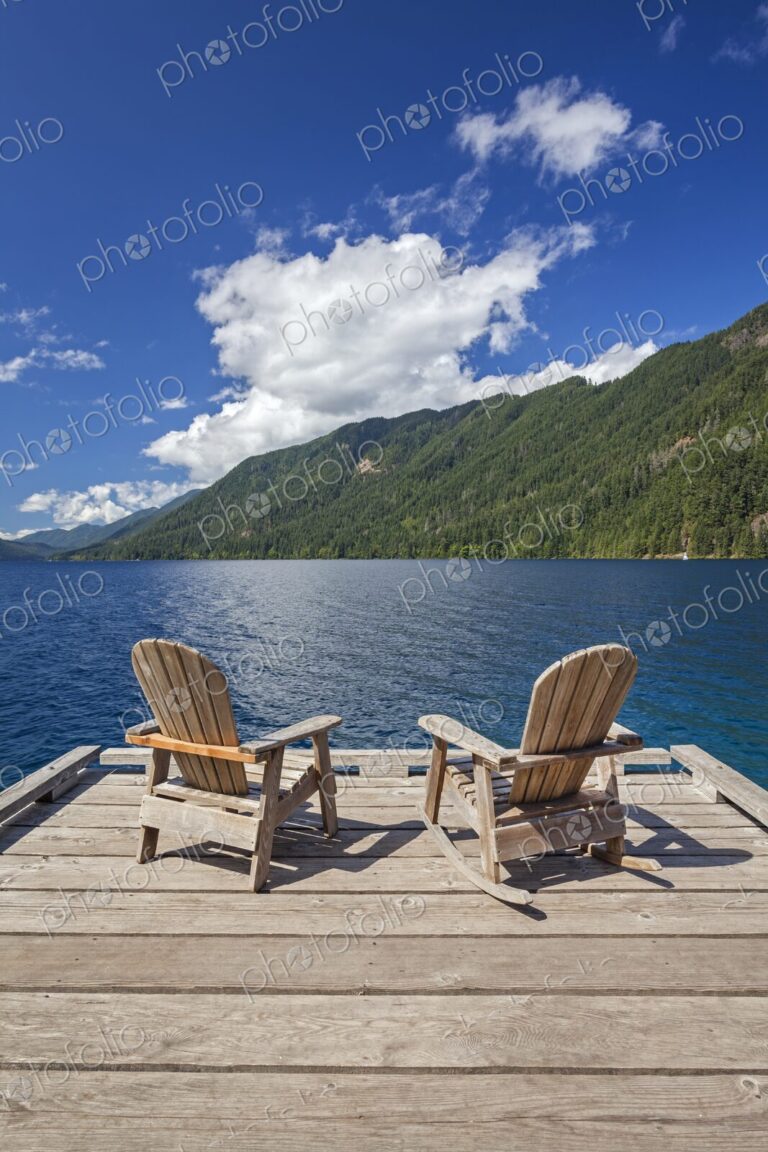 Two Adirondack chairs rest on a wooden dock with views of Lake Crescent and…