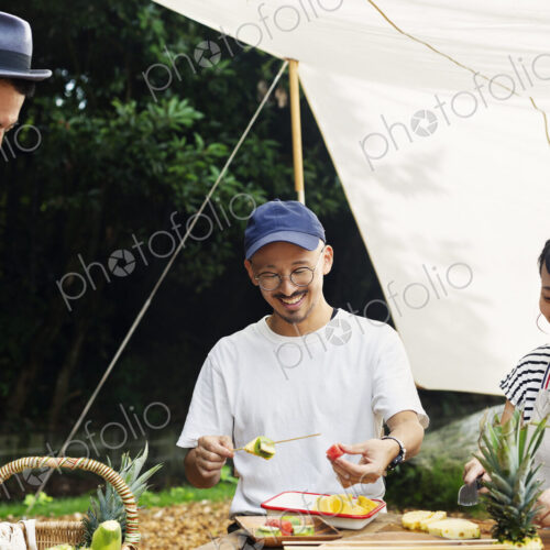 Two Japanese men and woman gathered around a table under a canopy, preparing fresh fruit.